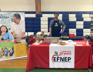 A young man stands behind an example table with the EFNEP logo.