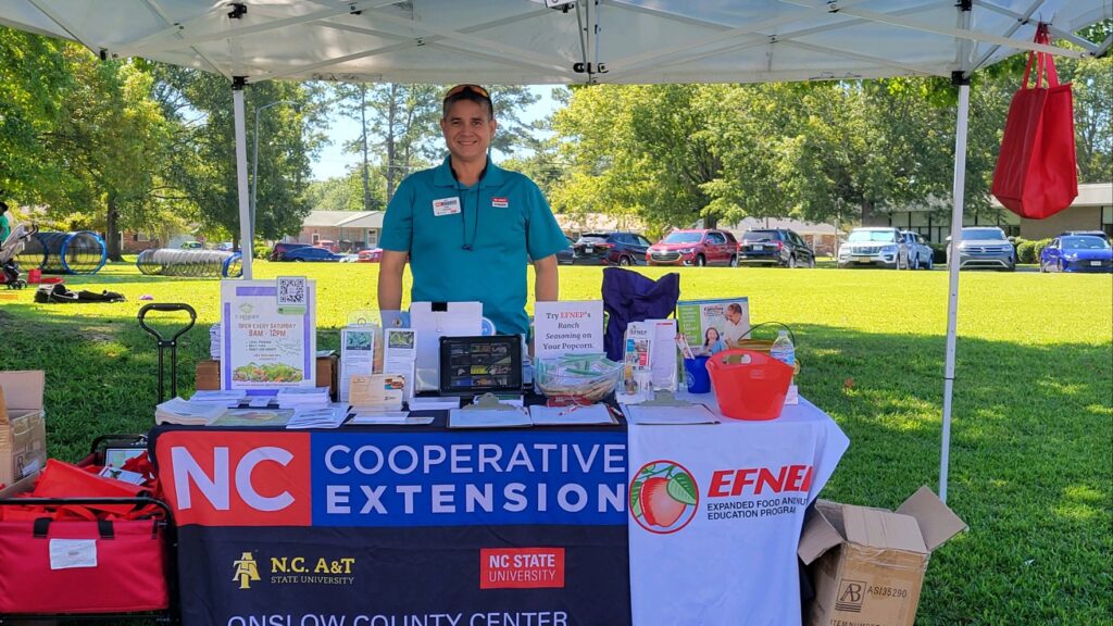 John stands behind N.C. Cooperative Extension info booth. 