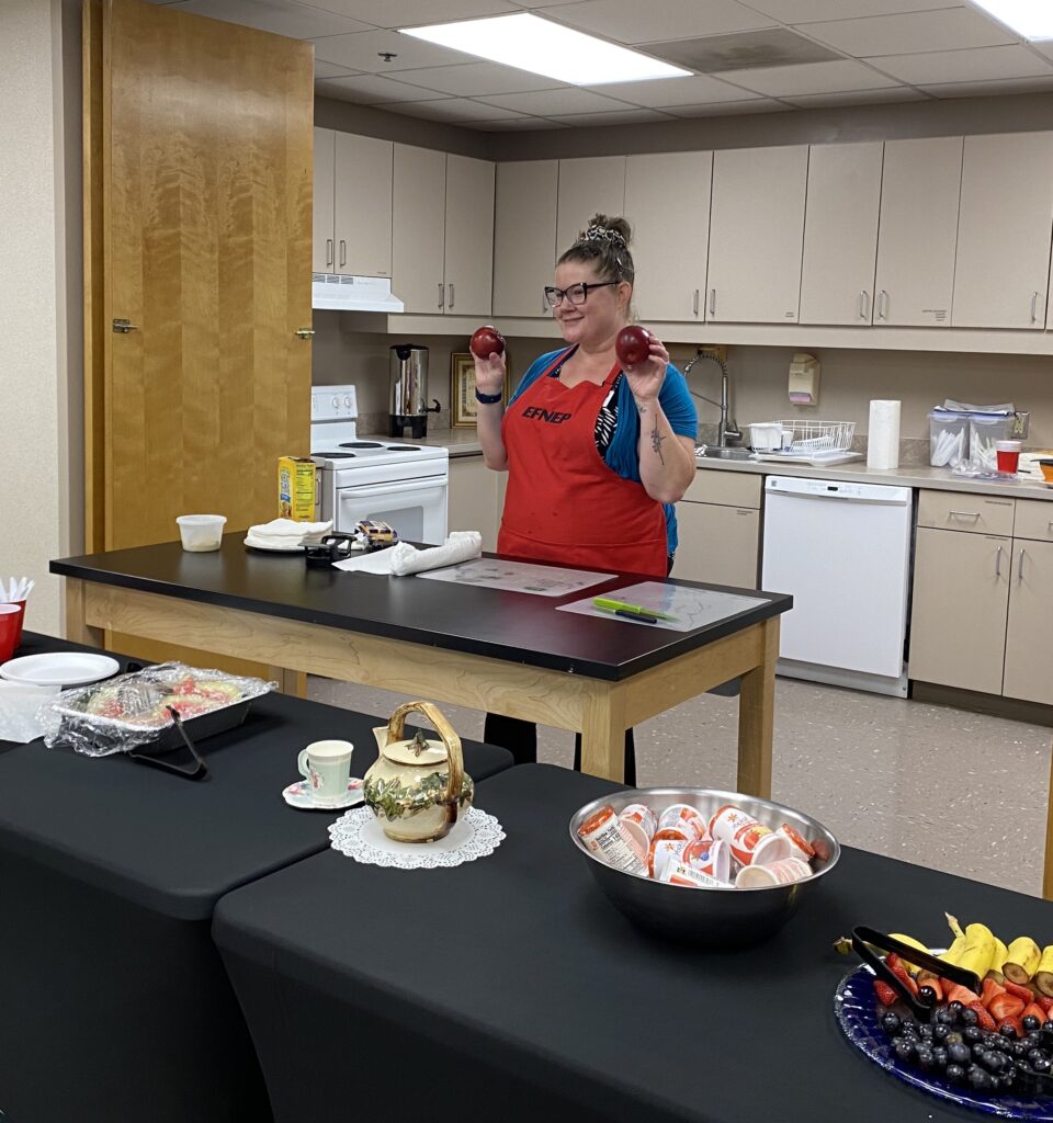 A woman shows two apples in a kitchen demonstration.