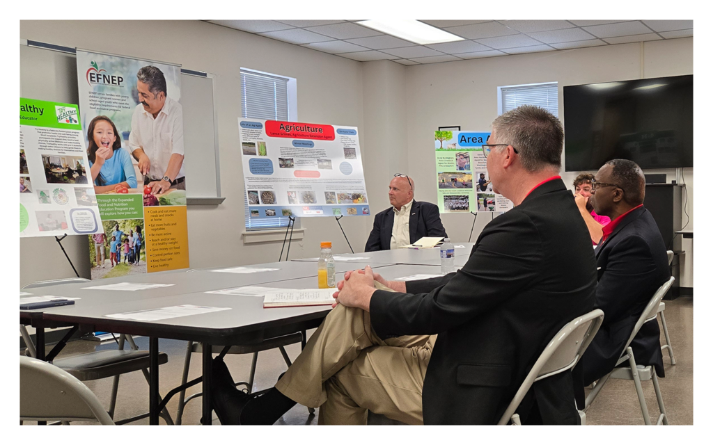 Dean Fox and Chancellor Howell witting in front of an EFNEP poster